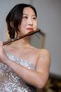 Asian woman in shiny dress playing flute and looking away