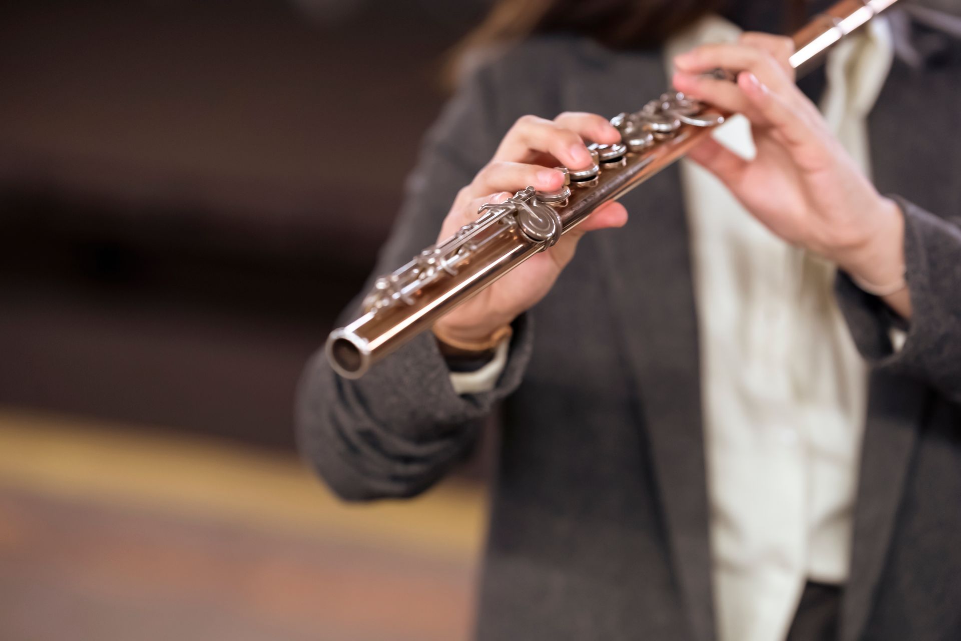 A woman elegantly playing a flute, showcasing musical talent and professional attire in a blurred background setting.