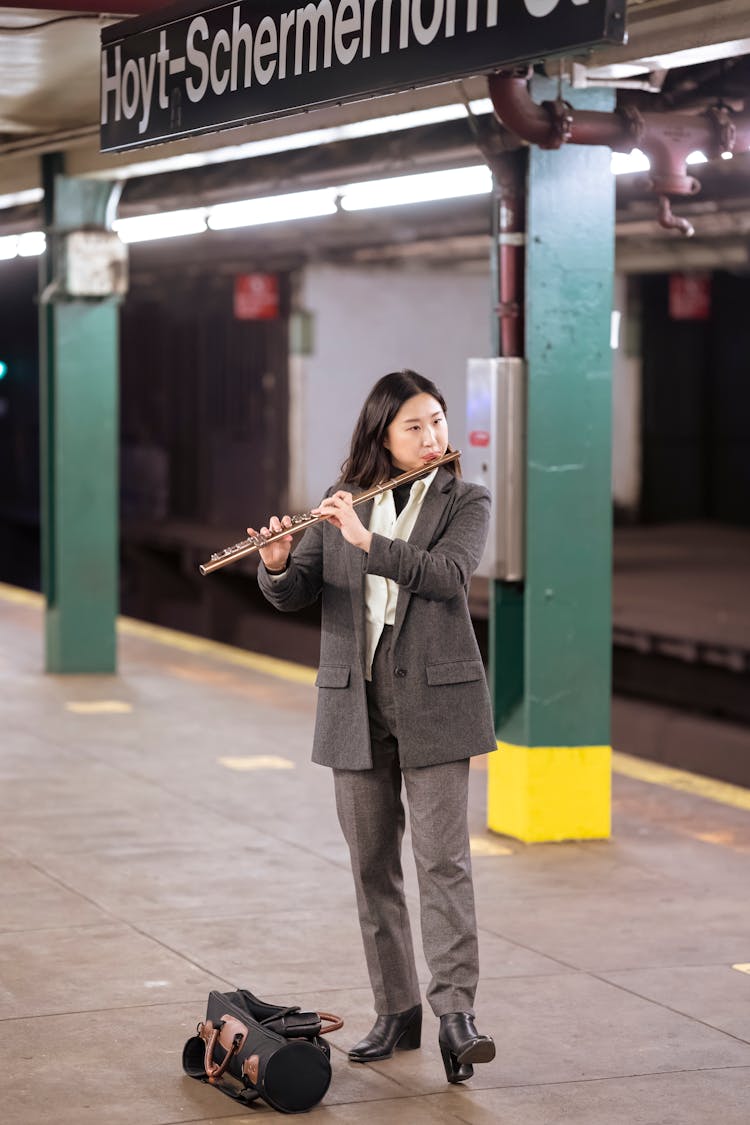 Asian Woman In Formal Suit Playing Flute In Subway