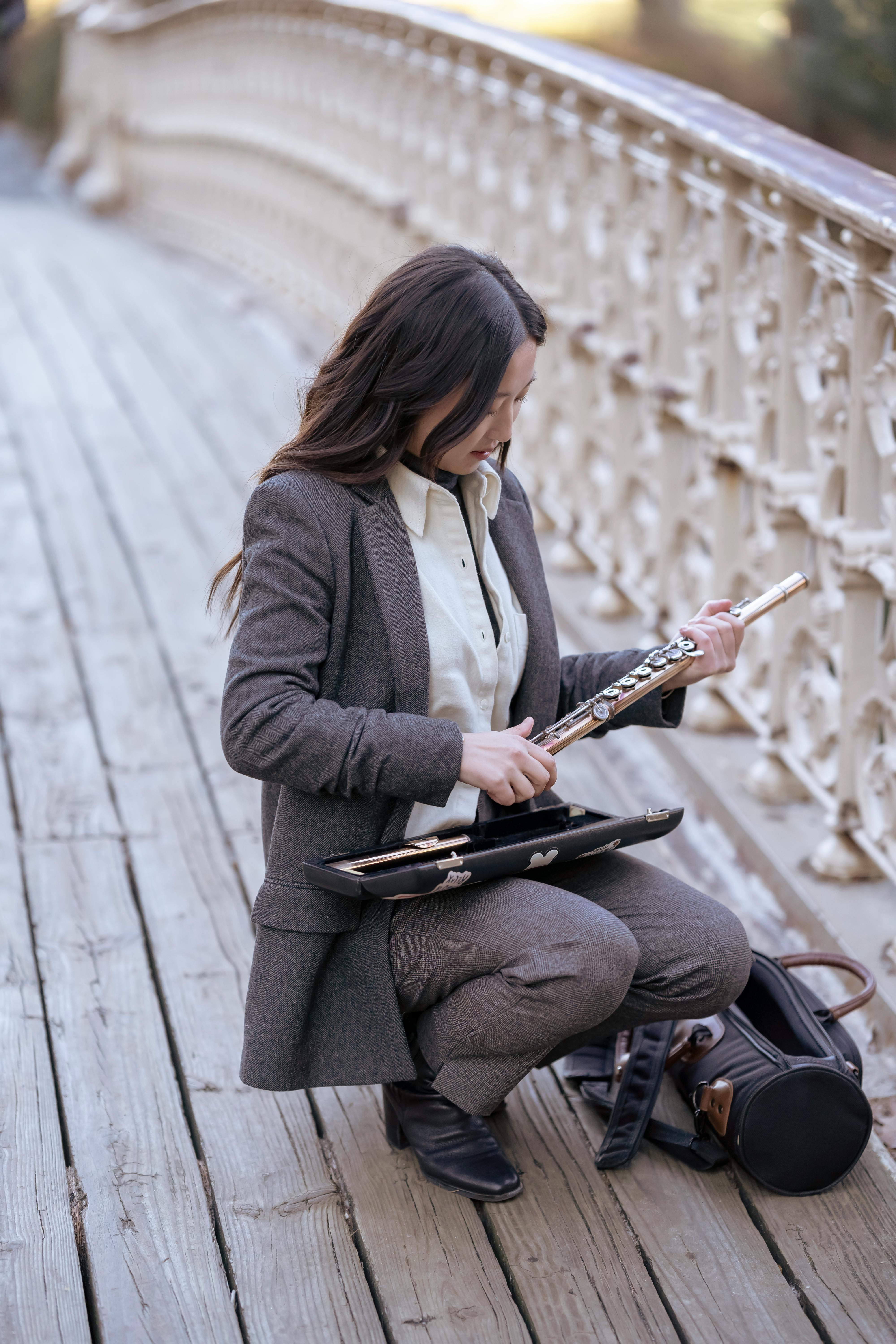 young asian musician squatting on plank footbridge and holding flute