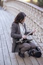 Young Asian female musician in gray suit and white blouse squatting on shabby plank footbridge and getting flute out of instrument case