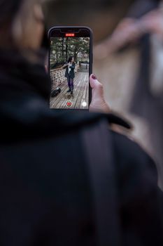 A person recording another with a smartphone outdoors on a wooden deck.