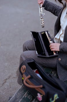 A woman assembles her flute while seated outdoors, dressed in elegant attire.