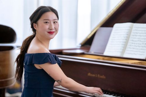 Free Side view of positive Asian female pianist in elegant dress pressing piano keys while practicing symphony and looking at camera Stock Photo