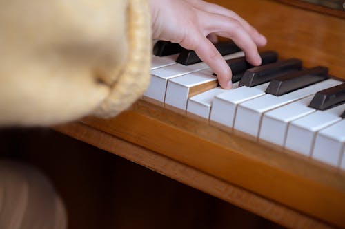 High angle of crop anonymous female pianist sitting at piano and pressing keys while practicing music