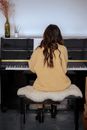 Back view full body of unrecognizable woman with long hair sitting on stool and playing piano