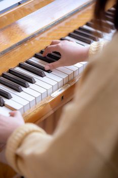 Crop unrecognizable female musician in beige clothes sitting at piano while playing melody in daytime