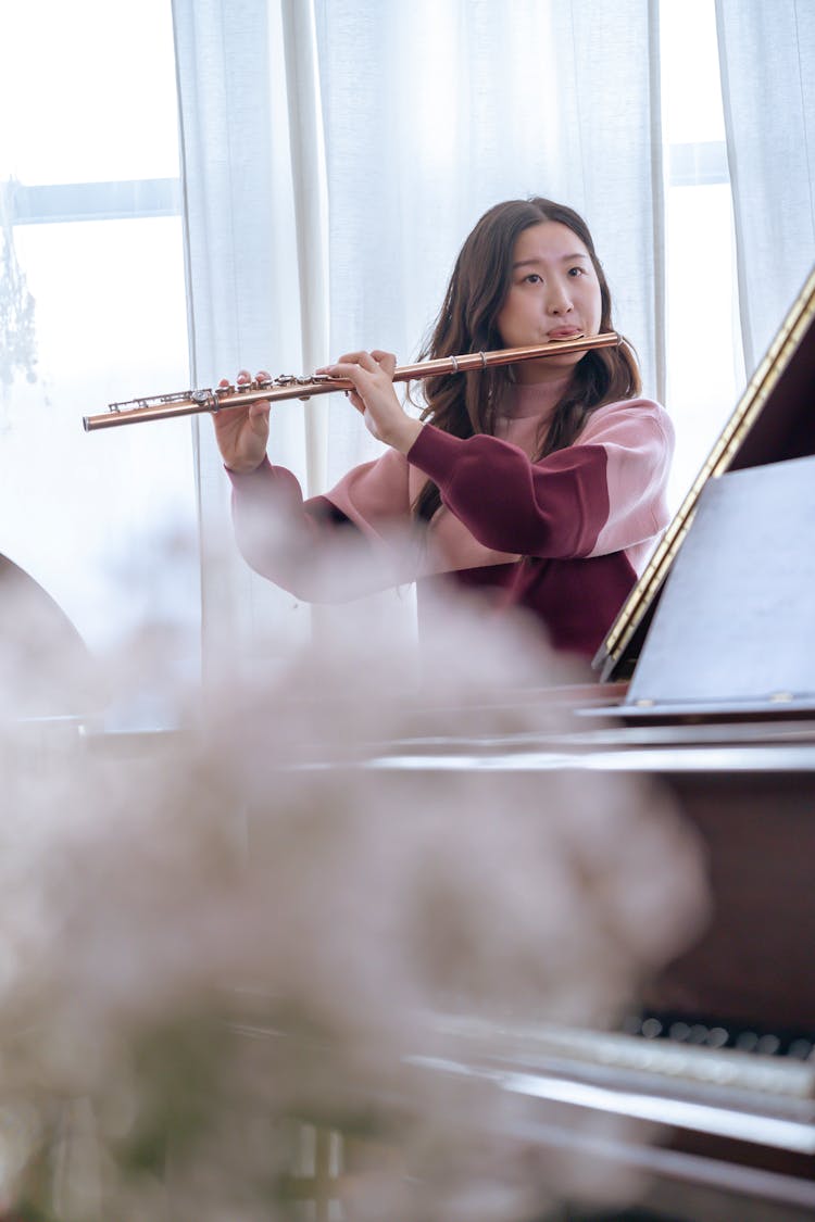 Asian Woman Playing Flute Near Piano In Studio