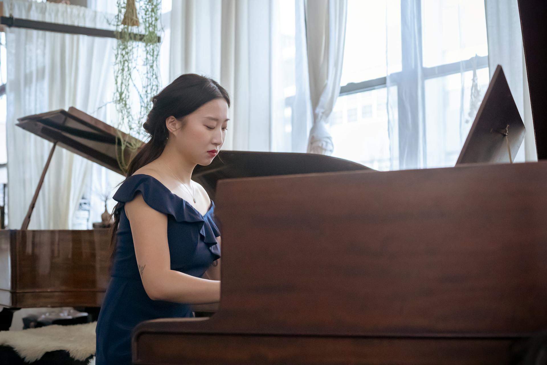 Ethnic female playing piano in room next to window