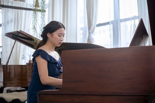 Free Concentrated young Asian woman in elegant dress playing piano while sitting in bright studio near windows with curtains Stock Photo