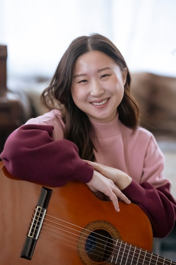 Smiling Asian Woman With Guitar In Studio