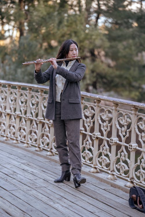 Serious Asian female playing flute in street on bridge