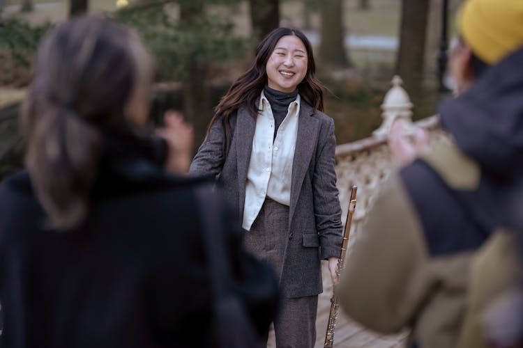 Smiling Asian Female Musician With Flute Near Crowd In Street