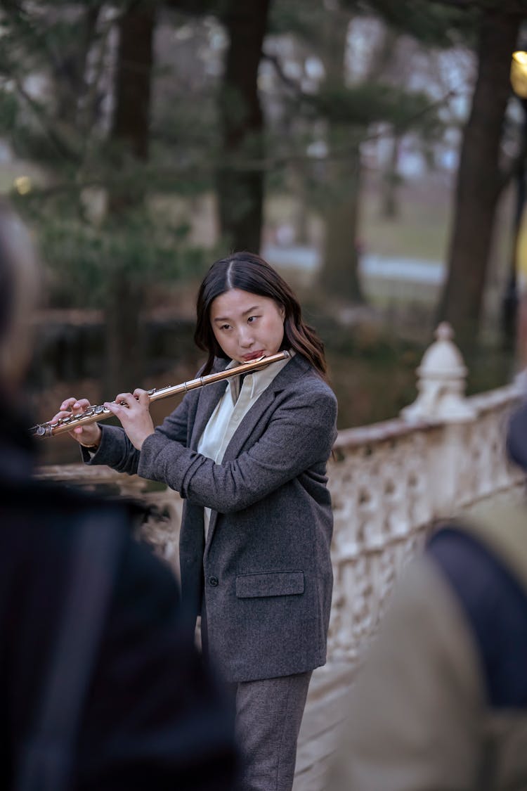 Asian Female Musician Performing On Flute Near Crowd In Street