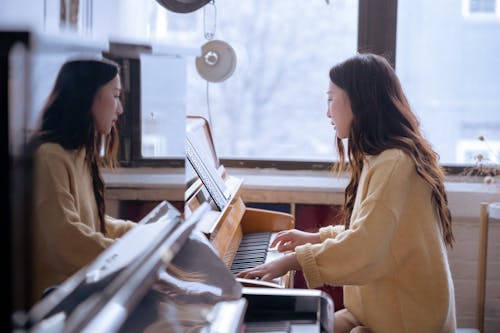 Side view of young ethnic female pianist playing piano while watching music score during rehearsal