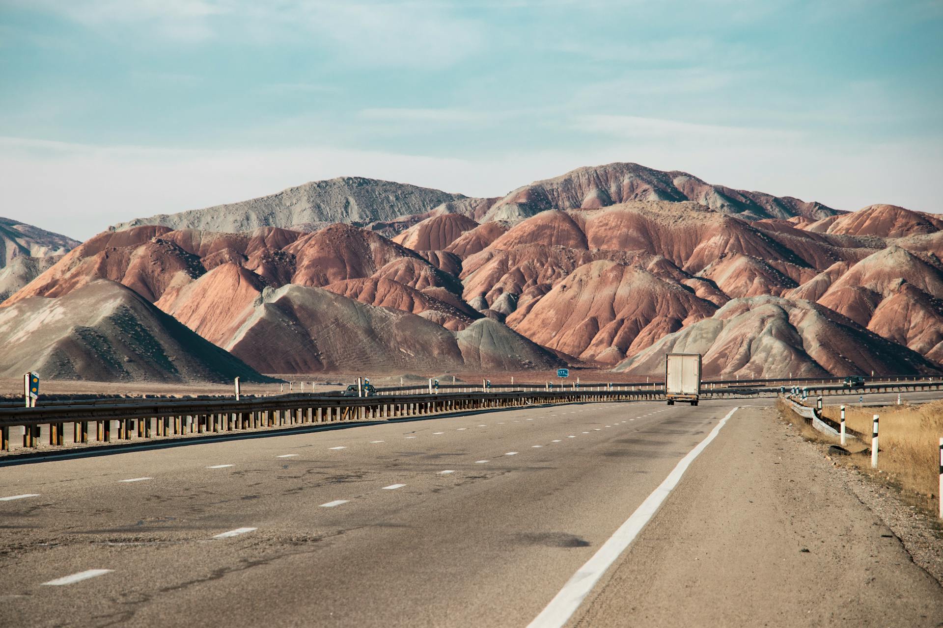 A highway cutting through a vibrant, arid mountain landscape with a distant truck on the road under a clear blue sky.