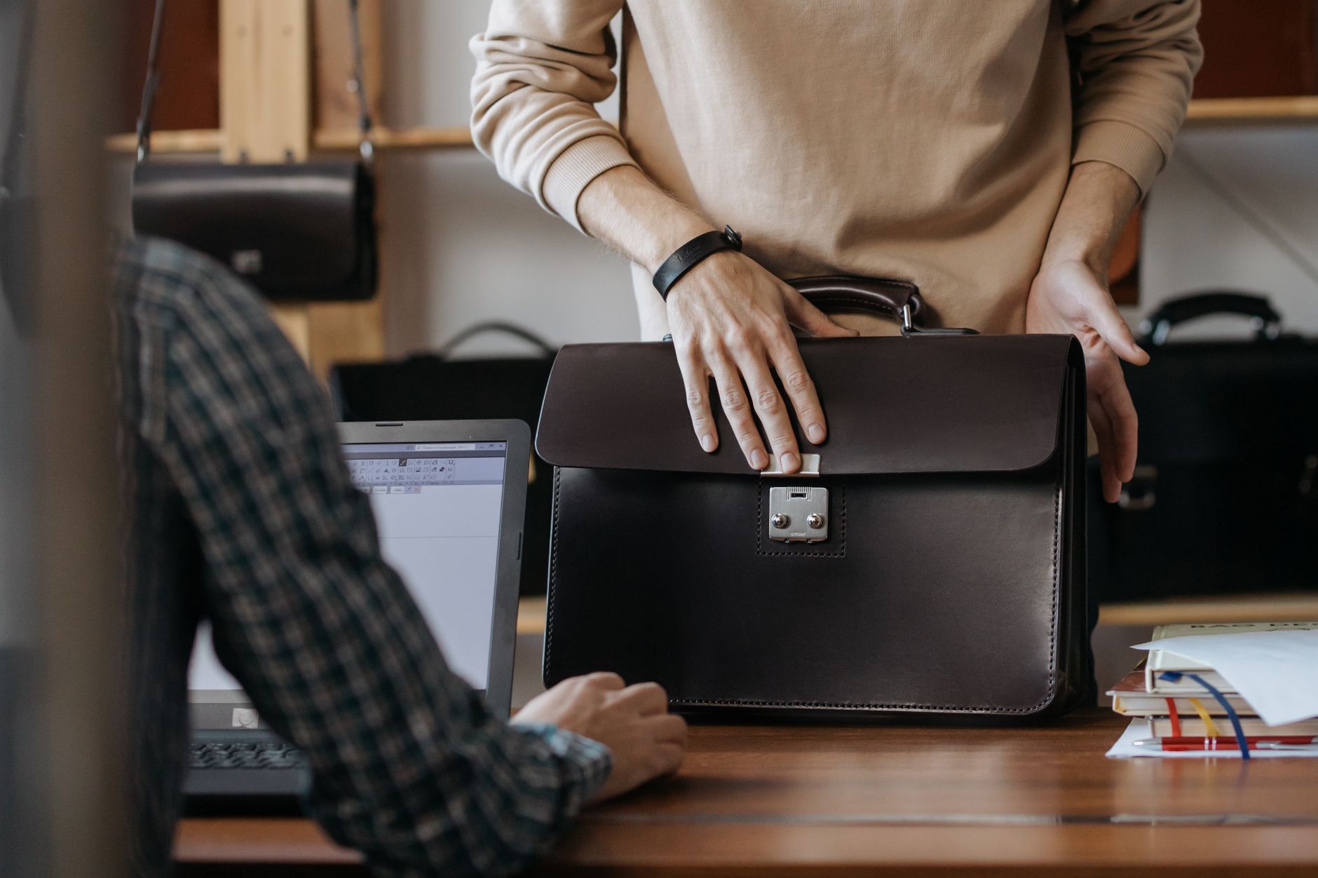 Close-up of two professionals handling a leather briefcase in an office setting.