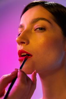 A woman getting lipstick applied with a brush in a beauty setting.