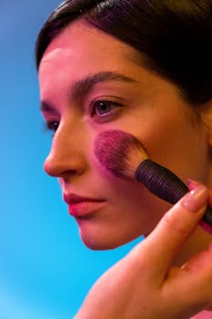Close-up of a woman applying makeup with a brush against a vibrant backdrop.