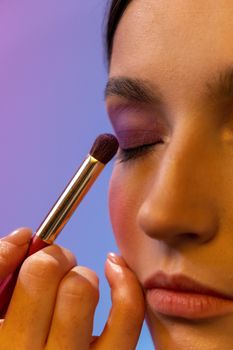 A woman applies purple eyeshadow with a makeup brush, showing a serene and artistic look.