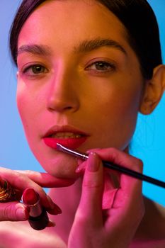 Close-up of a young woman getting her lipstick applied by a makeup artist.
