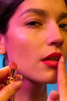 A young woman artistically applies lipstick in a vibrant close-up shot.