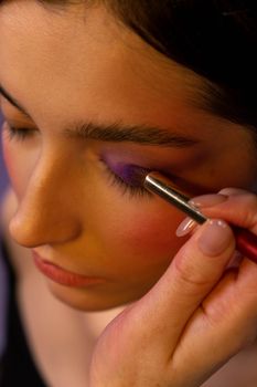 Close-up of a woman applying purple eyeshadow with a brush.