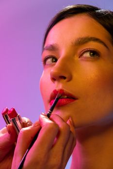 Elegant close-up of a woman applying lipstick with a makeup brush in a studio setting.