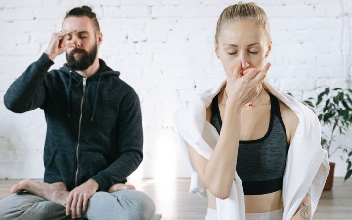 Two people meditating indoors, focusing on breathing exercises for relaxation and wellness.