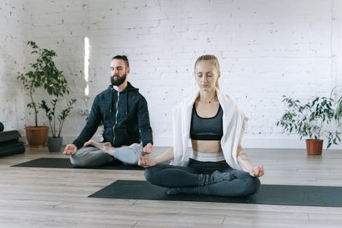 A Man and a Woman Sitting on Yoga Mat while Doing Yoga