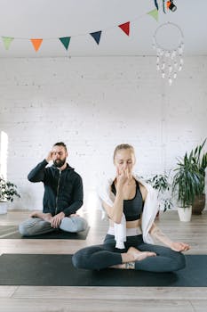 Two people practicing meditation and breathing on yoga mats indoors. Serene and relaxed setting.