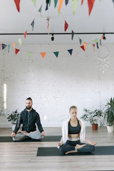 A man and woman practicing meditation in a serene yoga studio adorned with colorful flags.