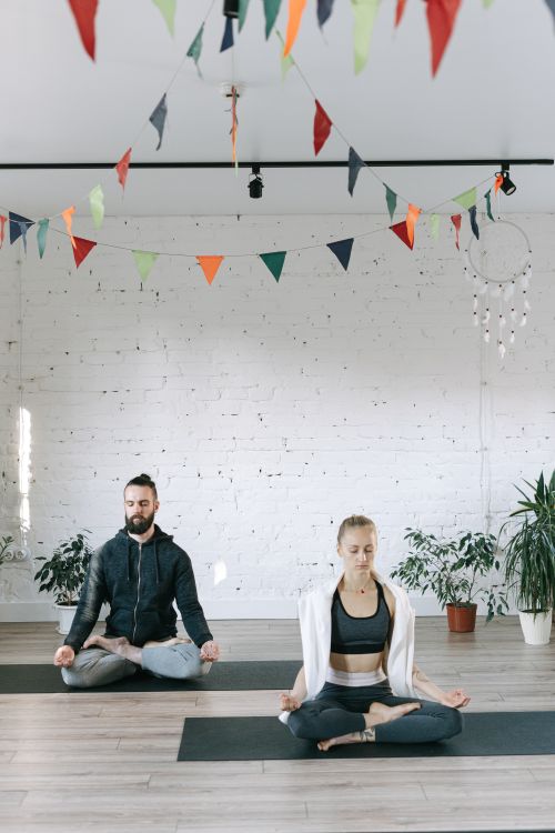 Free A man and woman practicing meditation in a serene yoga studio adorned with colorful flags. Stock Photo