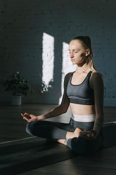 Serene adult woman practicing yoga indoors, meditating in lotus pose for wellness and relaxation.