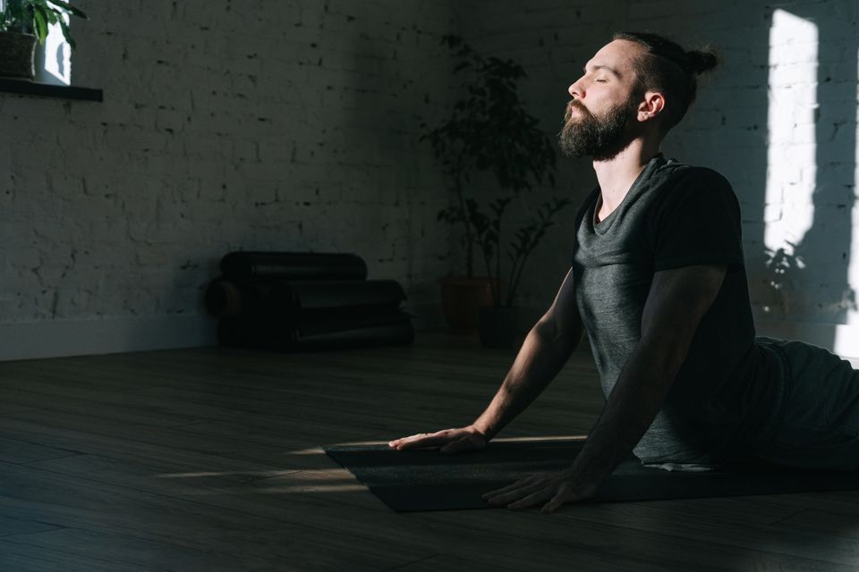 Bearded man sitting calmly on a yoga mat with eyes closed in a bright indoor space