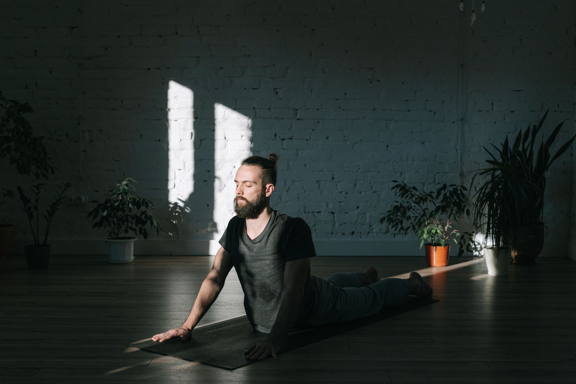 A man meditates indoors, bathed in sunlight, promoting tranquility and wellness.