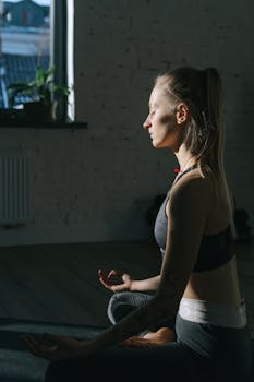 A woman is meditating indoors in a peaceful setting, focusing on mindfulness and serenity.