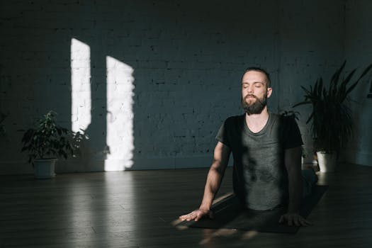 Bearded man practices yoga indoors with sunlight casting shadows, creating a tranquil environment.