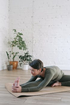 Woman in green activewear practicing yoga indoors, stretching on mat surrounded by plants.
