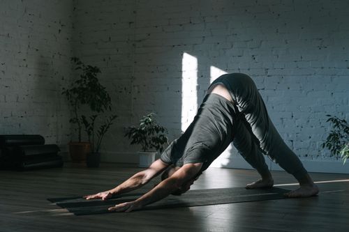 Free Adult man practicing yoga in downward dog pose on a mat indoors, emphasizing mindfulness and tranquility. Stock Photo