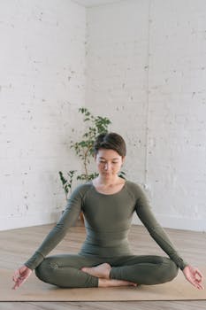 A serene woman meditates indoors on a yoga mat, practicing mindfulness and balance.