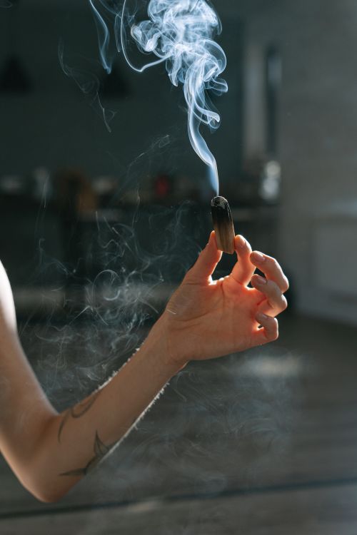 Free A hand holding a burning incense stick with smoke rising in a dark background. Stock Photo