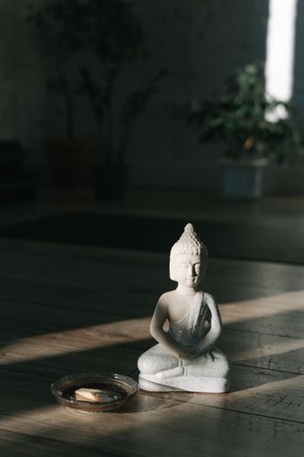 A peaceful Buddha statue sits on a wooden floor in a sunlit room, creating a calm atmosphere.