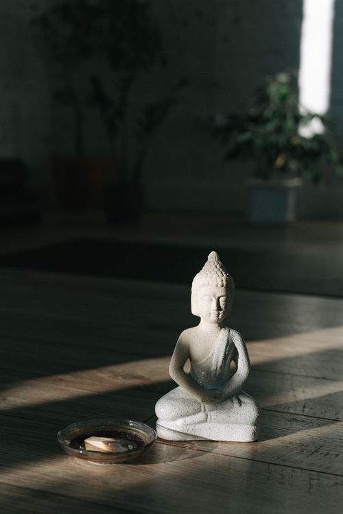 Free A peaceful Buddha statue sits on a wooden floor in a sunlit room, creating a calm atmosphere. Stock Photo