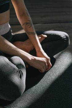 Close-up of a person sitting cross-legged indoors, showcasing a tattooed arm and yoga mat.