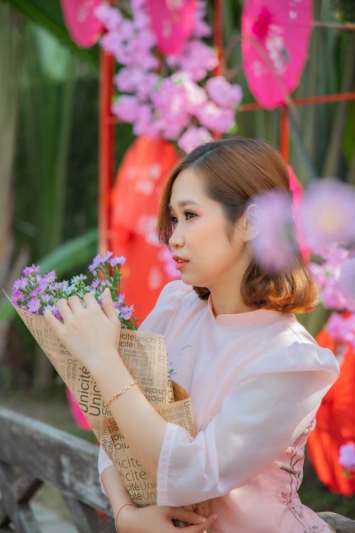 Free Asian woman in a pink dress holding a bouquet of flowers outdoors. Stock Photo