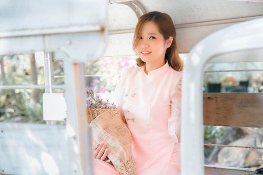 Charming woman in pink dress holding a bouquet, smiling gracefully in a rustic setting.