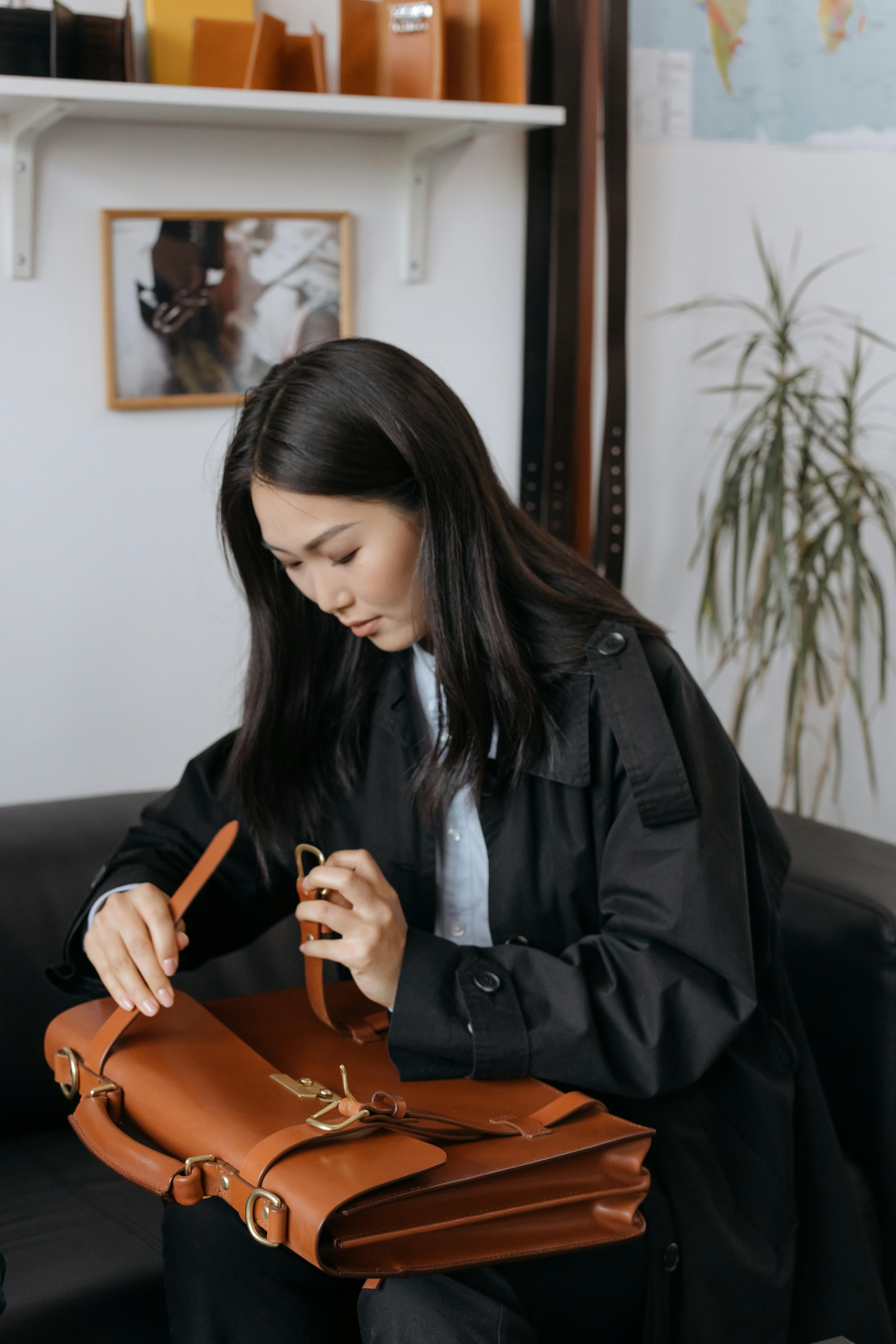 Businesswoman organizing a leather briefcase while sitting indoors, conveying a professional setting.