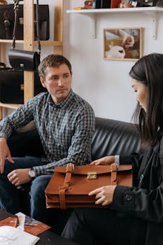 A man and woman discussing a leather briefcase in a stylish indoor setting.