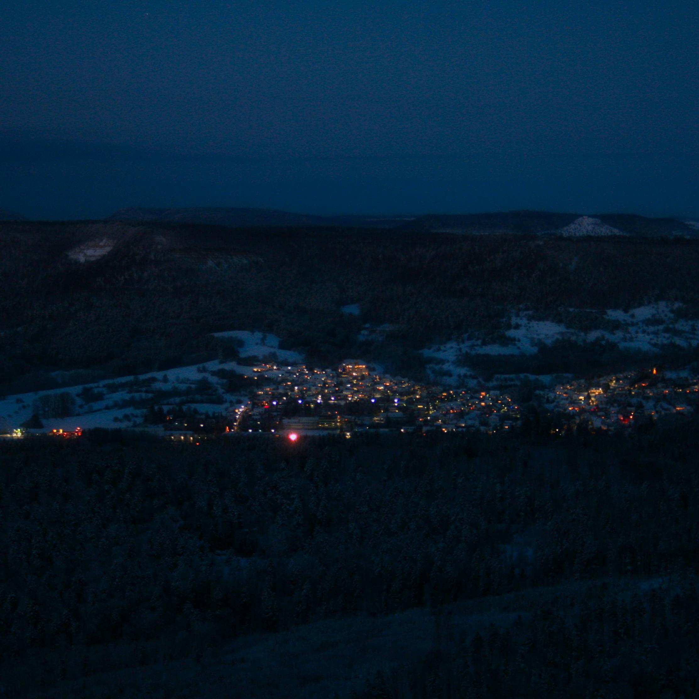 Aerial view of illuminated Albstadt town nestled in a snowy valley during a dark winter night.